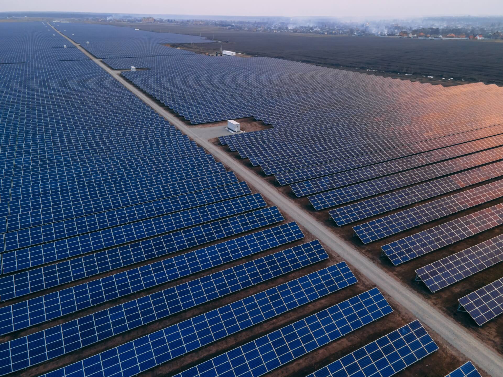 Aerial drone view into large solar panels at a solar farm at bright sunset. Solar cell power plants.